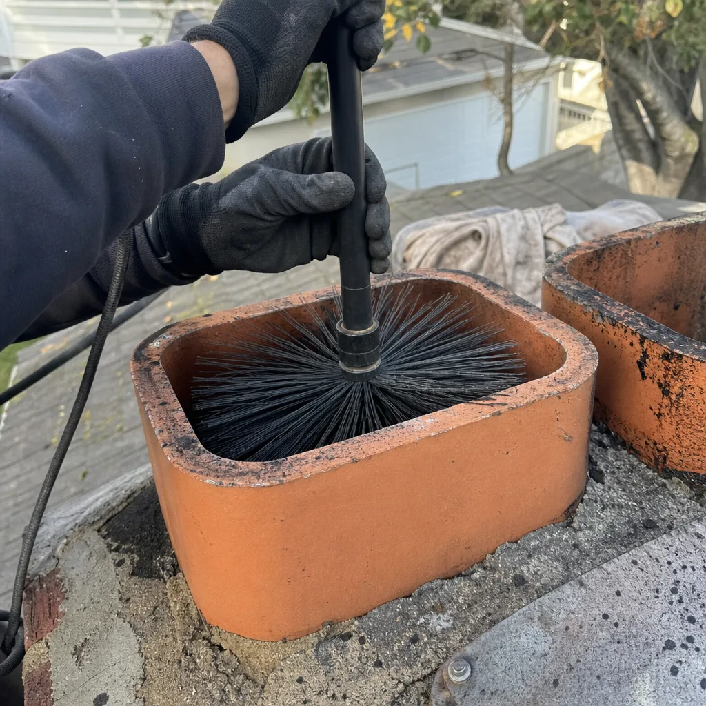 Professional chimney sweep cleaning a brick chimney flue with a wire brush.